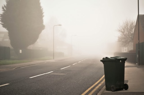 black wheelie bin by roadside on foggy day