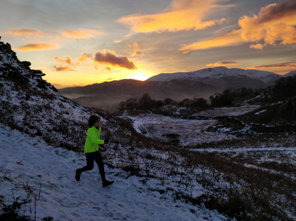 young boy wearing yellow jacket running along snowy mountain path at sunset