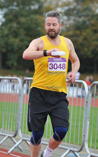 grey-haired man wearing yellow Cats Protection t-shirt looking at watch while running