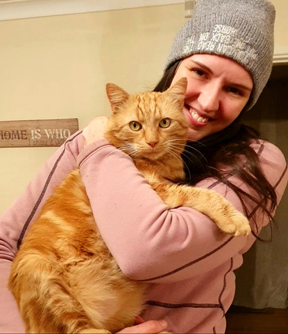 Brunette woman in pink jumper and grey hat holding ginger tabby cat
