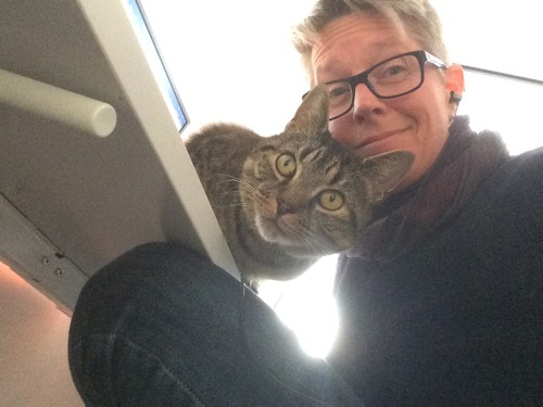 short-haired woman wearing glasses next to brown tabby cat