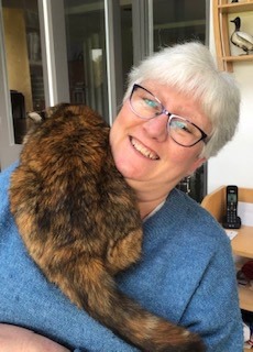 grey-haired woman with glasses with brown cat lying on her shoulder