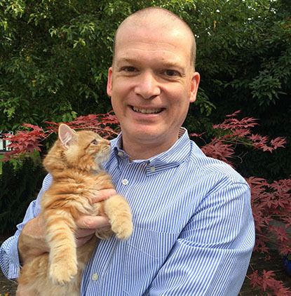 man wearing blue-and-white striped shirt holding ginger tabby cat