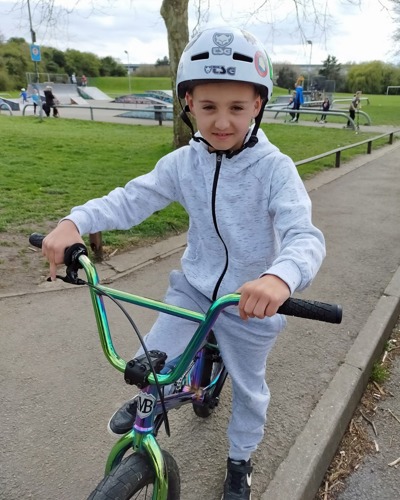 Young boy wearing grey tracksuit and white helmet on BMX bike