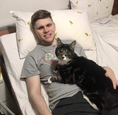 Young man with short brunette hair lying on bed with tabby-and-white cat lying on his chest