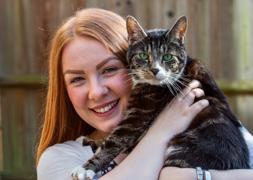 red-haired young woman holding brown tabby-and-white cat