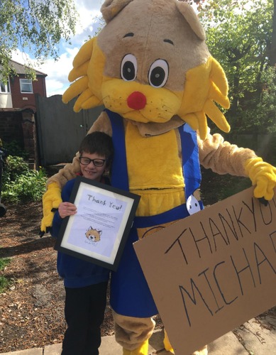 Persona in costume da mascotte di gatto con un braccio intorno a un giovane ragazzo bruno dai capelli corti che tiene in mano un certificato di ringraziamento thank