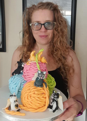 woman with long curly blonde hair holding cake shaped like balls of wool and cats