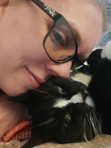 woman wearing glasses with face up against face of black-and-white cat