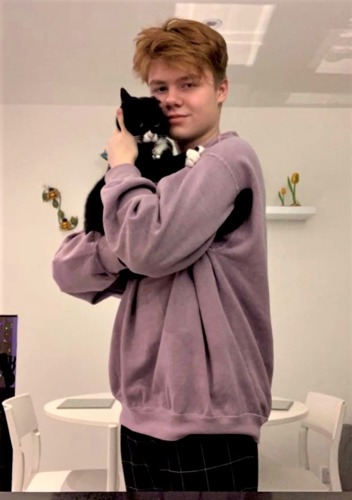 Short-haired brunette teenage boy wearing purple jumper and holding black-and-white cat