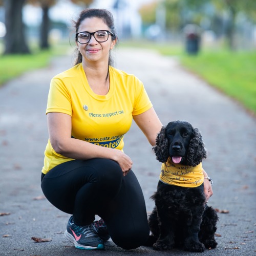 long-haired brunette woman wearing yellow Cats Protection t-shirt next to black cocker spaniel dog