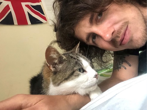 Brunette man with tabby-and-white cat lying on his arm