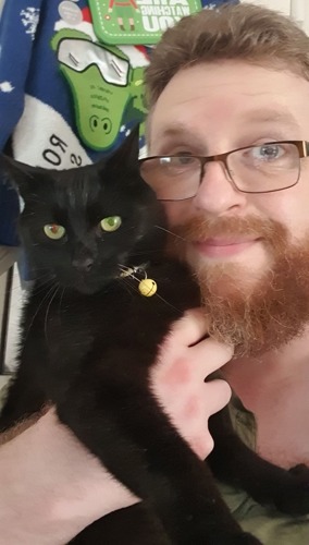 brunette man with beard holding black cat next to his face