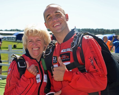 blonde woman and bald man wearing red flight suits and giving thumbs up