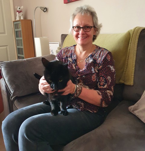 grey-haired woman sitting on sofa with black cat on her lap