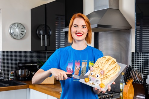 woman with short red hair holding cake shaped like a cat