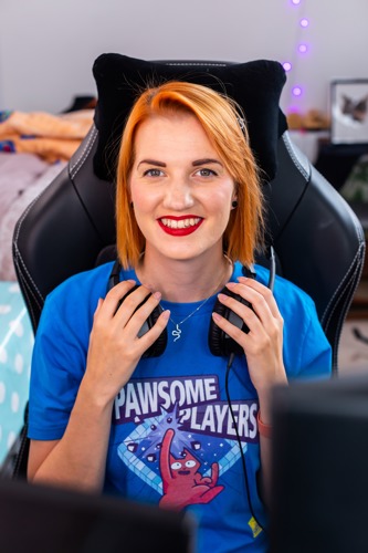 woman with short red hair wearing headphones around her neck and a blue Pawsome Players t-shirt