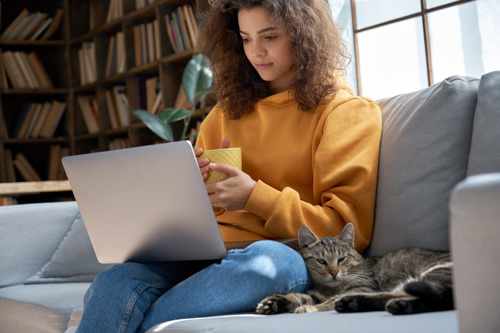 brown tabby cat sat on a sofa next to a woman with a laptop on her lap