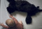 A long-haired black cat lying stretched out on a bed beside a baby wearing a pink knitted top.