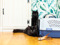 a black cat lying on the floor next to a plastic cat carrier. Another black cat is blurred in the background