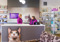 Two people talking at a charity shop counter surrounded by shelves of donated goods.