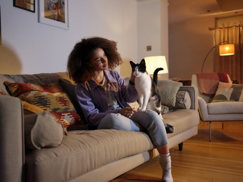 black woman with afro hair sitting on a sofa with a black-and-white cat on her knee