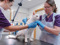 White cat standing on a vet examination table while two veterinary staff examine them.